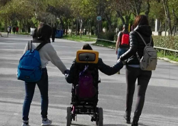 ragazzo in carrozzina che passeggia con amiche che lo tengono per mano